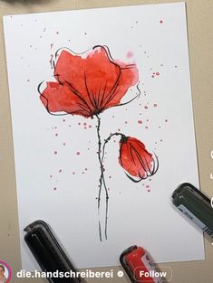 a red flower painted on white paper next to some markers