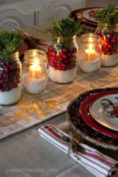 candles are lit in small mason jars filled with berries and greenery on a table