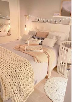 a white bed with blankets and pillows on top of it in a bedroom next to a baby crib