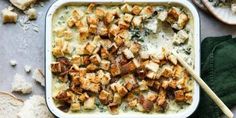 a casserole dish with chicken and spinach in it on a table next to bread