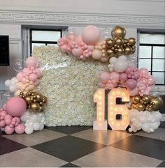 a large number surrounded by balloons and flowers in front of a wall with the number 16 on it