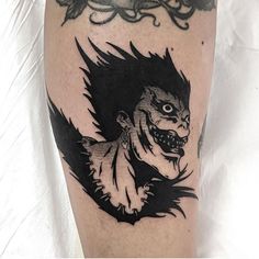 a black and white photo of a demon tattoo on the right leg with an evil face