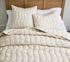 an unmade bed with white linens and pillows on top of the headboard