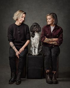 two women sitting next to each other with a dog in front of them on top of a suitcase