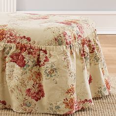 a flowered bed skirt on top of a footstool in front of a window