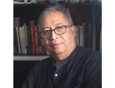 a man with glasses sitting in front of a bookshelf