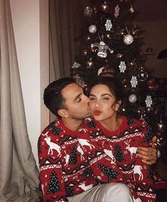 a man and woman sitting in front of a christmas tree wearing matching ugly sweaters