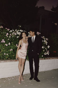 a man and woman standing next to each other in front of some flowers at night