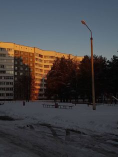 an apartment building in the distance with snow on the ground and trees around it at sunset