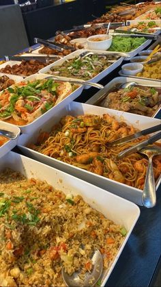 many trays of food are lined up on a table with utensils and spoons