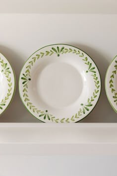 three green and white plates sitting on top of a shelf