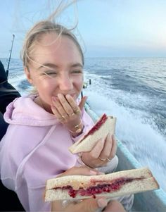 a woman eating a sandwich while on a boat in the ocean with another person behind her