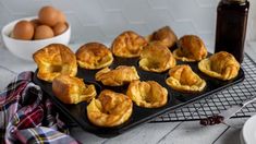 baked pastries on a baking tray next to a bowl of eggs and a bottle of syrup