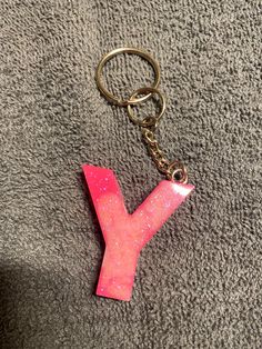 a pink letter shaped keychain sitting on top of a gray carpeted floor