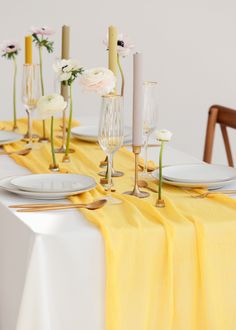 the table is set with yellow linens and white plates, silverware, and flowers