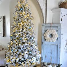 a white christmas tree with blue and silver ornaments on it in a living room next to an old door