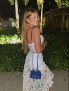 a woman wearing a white dress and holding a blue handbag in her right hand