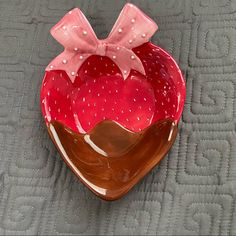 a strawberry shaped bowl with a pink bow on the top and brown base, sitting on a quilted surface