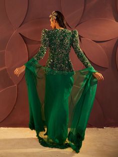 Editor's Note Featuring a regal emerald green floral embroidered peplum shoulder puffed jacket fitted on the upper body. Paired with a draped skirt & fringe dupatta. Color: Green Fabric: Tulle, silk organza, lining: silk Embroidery details: Zari And dabka Fit: Fitted Neck type: Sweetheart Sleeve type: Full sleeves Component: Skirt, peplum jacket top, dupatta Occasion: Sangeet and Wedding Guest Care: Dry clean only Note: Can be customised in any color from designers color palette About the Design Fringe Dupatta, Puffed Jacket, Skirt Fringe, Puff Blouse, Green Drapes, Tulle Embroidery, Green Tulle, Puff Jacket, Peplum Jacket