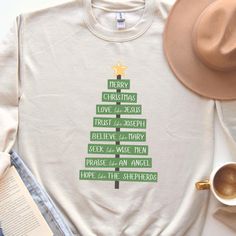 a white shirt with a green christmas tree on it next to a hat and coffee cup