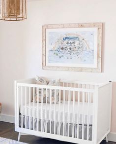 a white crib in the corner of a room with a painting on the wall