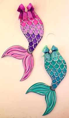 two colorful mermaid tail earrings with bows on them, one is pink and the other is blue