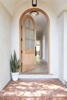 an arched wooden door is open to a hallway with tile flooring and potted plant