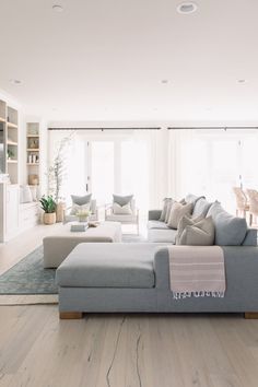 a living room filled with lots of furniture and white walls in front of large windows