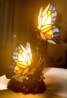 two stained glass butterflies sitting on top of a wooden table next to a light bulb