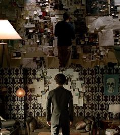 a man standing in front of a wall covered with pictures and papers on the walls