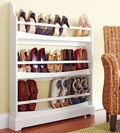 a white shoe rack filled with shoes next to a brown chair and yellow wall behind it