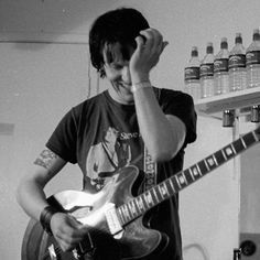 a young man holding his head while playing an electric guitar in a room with bottles on the wall