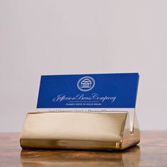 a gold business card holder sitting on top of a wooden table next to a white wall