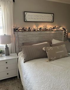 a white bed topped with lots of pillows next to a night stand and window sill