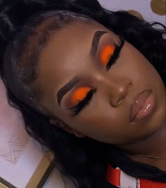 a woman with bright orange eyeshadow laying on top of a table next to a book