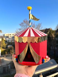 a person holding up a red and white box with a circus tent on it's roof