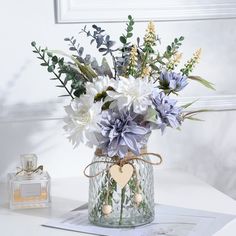 a vase filled with lots of flowers on top of a white table next to a perfume bottle