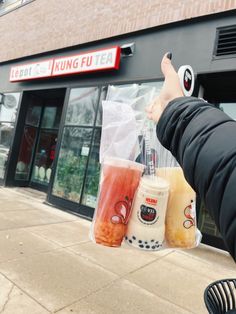 a person holding two drinks in front of a coffee shop with their hand on the bag