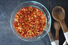 a glass bowl filled with spices next to two wooden spoons