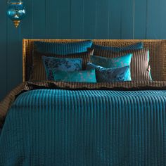 a bed with blue comforters and pillows in a teal colored room, next to a hanging lamp