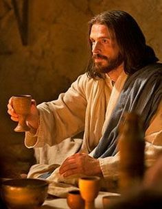 jesus holding a cup in his hand while sitting at a table with other items on it