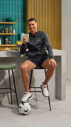 a man sitting at a table with a soccer ball in front of him holding a drink