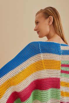 a woman is wearing a multicolored crocheted shawl and has her back turned to the camera