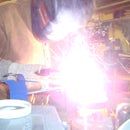 a man working on something with a grinder in front of him and another person sitting at a table behind him