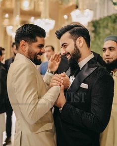 two men standing next to each other in suits and ties, one holding the other's hand