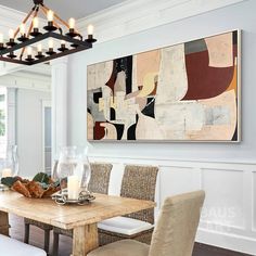 a dining room table and chairs in front of a painting on the wall above it