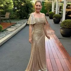 a woman wearing a gold dress standing on a wooden deck in front of some bushes