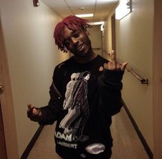 a man with pink dreadlocks standing in a hallway holding his hand out to the side