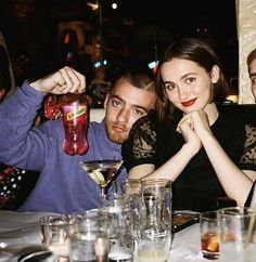 two people sitting at a table with drinks in front of them and one person holding up a drink