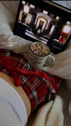 a person laying in bed with a cup of coffee on their lap and a laptop